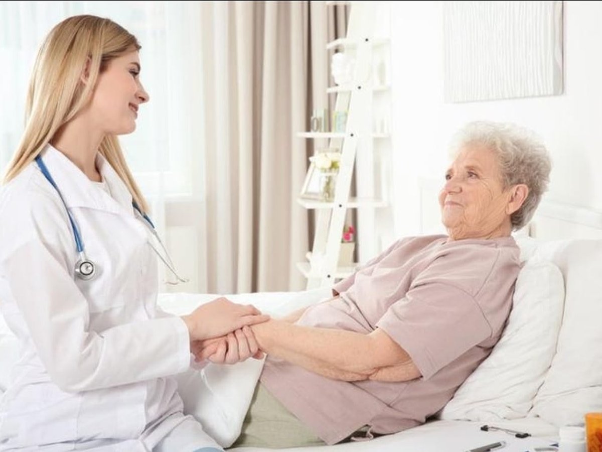 A caregiver holding the hand of an older patient resting in bed